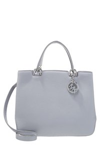 Bolso de mano de piel gris claro con dos asas, una correa de hombro desmontable y un charm redondo de logo plateado MK colgando de una de las asas.