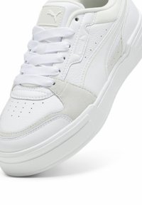 Baskets basses blanches Puma en cuir texturé, détails en daim, perforations, semelle épaisse et lacets blancs.