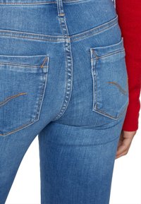 Vaqueros de mezclilla azul de tiro alto con dos bolsillos traseros, cosidos con hilo naranja, que cuentan con una textura suave y un diseño ajustado.