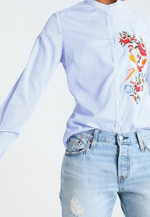 Hellblau-weiß gestreiftes Hemd mit bunter Blumenstickerei kombiniert mit hell gewaschenen, zerrissenen Jeans.