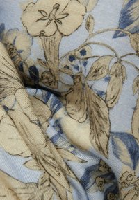 Tela suave con un estampado floral detallado en tonos beige y azul, que muestra flores, hojas y tallos con líneas finas y tejido texturizado.