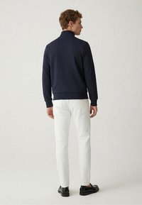 Marineblauer Sweatshirt mit hohem Kragen, lockerem Schnitt; kombiniert mit weißen Hosen und schwarzen Schuhen. Glatte Textur, minimalistisches Design.