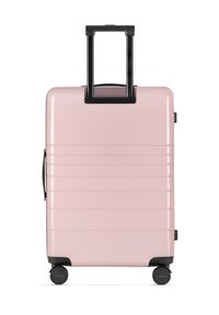 Valigia rigida rosa con righe verticali, dettagli neri, maniglia retrattile e quattro ruote per facilitare il movimento. Design compatto e strutturato.