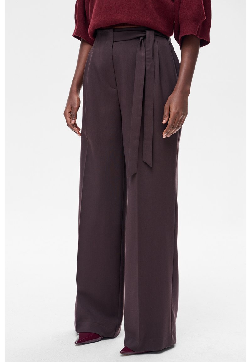 Spodnie z wysokim stanem i szerokimi nogawkami w ciemnym bordowym materiale o gładkiej fakturze, wyposażone w pas wiązany w talii w tym samym kolorze.