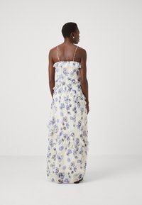 Lang, blomstret maxikjole med hvit bunn og blå-lilla blomsterprint. Har volanger og tynne justerbare stropper. Lett stoff.