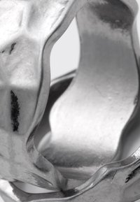 Gros plan d'une sculpture en métal argenté torsadée et réfléchissante, avec des courbes lisses et fluides et une surface texturée.