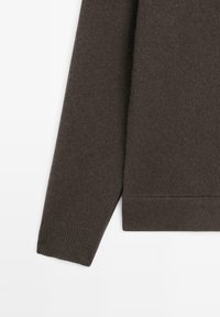 Tmavě hnědý pletený svetr s rukávem a žebrovaným lemem na bílem pozadí, ukazující texturu látky a okraj oděvu.