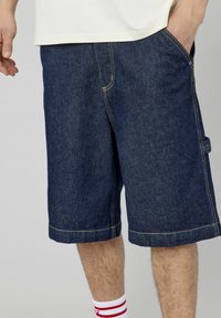 Shorts en denim bleu foncé, avec une coupe décontractée, des détails de couture visibles, des poches sur les côtés et à l'avant, et une longueur au genou.