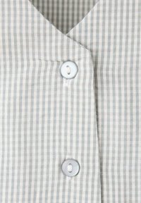Gros plan d'un tissu rayé vertical gris clair et blanc avec deux boutons blancs fixés sur un vêtement.