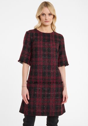 Red and black plaid dress made from textured fabric. Features short, fringed sleeves and a fitted silhouette with a flared hem.
