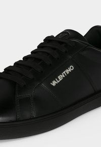 Baskets en cuir noir avec lacets noirs, logo Valentino blanc sur le côté et design à bout arrondi.