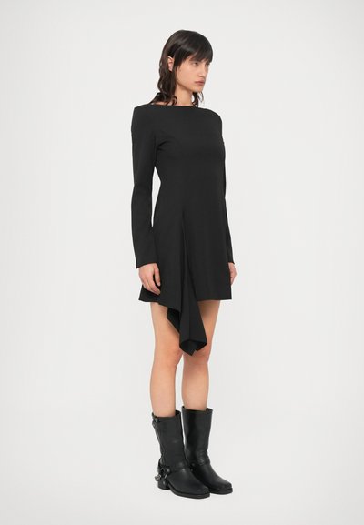Čierne dlhé šaty s člnovým výstrihom, asymetrickým lemom a hladkou textúrou, doplnené čiernymi koženými čižmami po kolená.