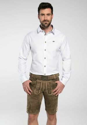Das weiße Langarmhemd zeichnet sich durch ein Knopfdesign und dunkle Knöpfe aus und wird mit braunen Lederhosen kombiniert, die dekorative Nähte und Taschen haben.
