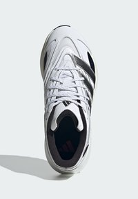 White athletic shoe with a textured upper, black stripes, and a cushioned interior. Features laces and a rounded toe design.