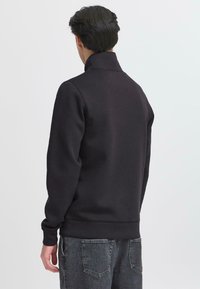 Hanorac negru cu guler înalt, manșete și talie ribbed. Material moale cu o textură netedă, conceput pentru o potrivire relaxată.