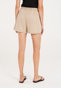 Beżowe bawełniane szorty z elastycznym pasem, dwiema tylnymi kieszeniami i luźnym krojem, charakteryzujące się gładkim, teksturowanym materiałem oraz wykończeniem brzegów.