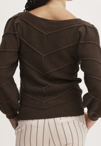 Brown knit sweater with a chevron pattern, featuring a wide neckline and puffed sleeves. Ribbed cuffs and hem provide texture.
