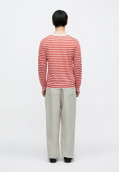 Μακρυμάνικο πουκάμισο με κόκκινες και λευκές ρίγες και στρογγυλή λαιμόκοψη, σε συνδυασμό με ανοιχτό γκρι λινά παντελόνια με δύο πίσω τσέπες.