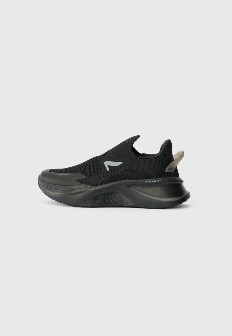 Chaussure de sport noire à enfiler avec semelle épaisse, dessus en mesh respirant, languette au talon et logo réfléchissant sur le côté sur fond uni.