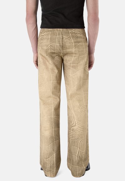 Personne portant un pantalon ample à carreaux beige et un haut noir à manches courtes, vue de dos sur un fond uni.