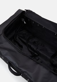 Crni duffel torba sa munjevitim otvaranjem, glatkom vanjskom površinom, podesivim remenima unutra i mrežnim džepom na vrhu za organizaciju.