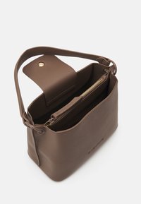 Brun läderhandväska med en strukturerad design, en platt axelrem, en innerväskficka med dragkedja och ett magnetlås.