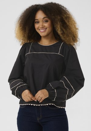 Schwarze Bluse mit Puffärmeln, ausgestattet mit einer weißen gewellten Bordüre entlang des Ausschnitts und der Bündchen. Aus glattem Stoff mit leichtem Glanz hergestellt.