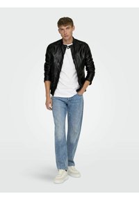 Zwarte leren jas met textuur, witte T-shirt, lichtblauwe recht gesneden jeans en forse witte sneakers.