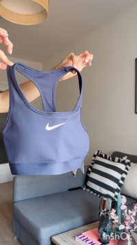 Χέρια κρατούν ένα μπλε αθλητικό σουτιέν Nike σε ένα σαλόνι με έναν γκρι καναπέ και μια ριγέ μαξιλαροθήκη στο βάθος.