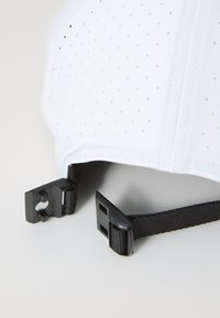 Hvitt cap med perforert design, sort justerbar stropp og klips for tilpasning. Glatt tekstur med strukturert form og ren søm.