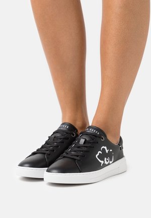 Sorte lædersneakers med hvidt blomsterdesign, rund tå, flad hvid sål og klassisk snøredesign.