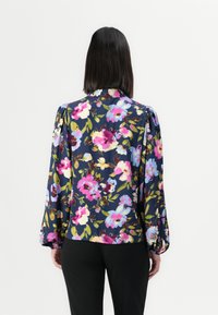 Blomstrete bluse med lange ermer, med en mørk marineblå bakgrunn og livlige mønstre av rosa, blå og grønne blomster. Mykt stoff og avslappet passform.