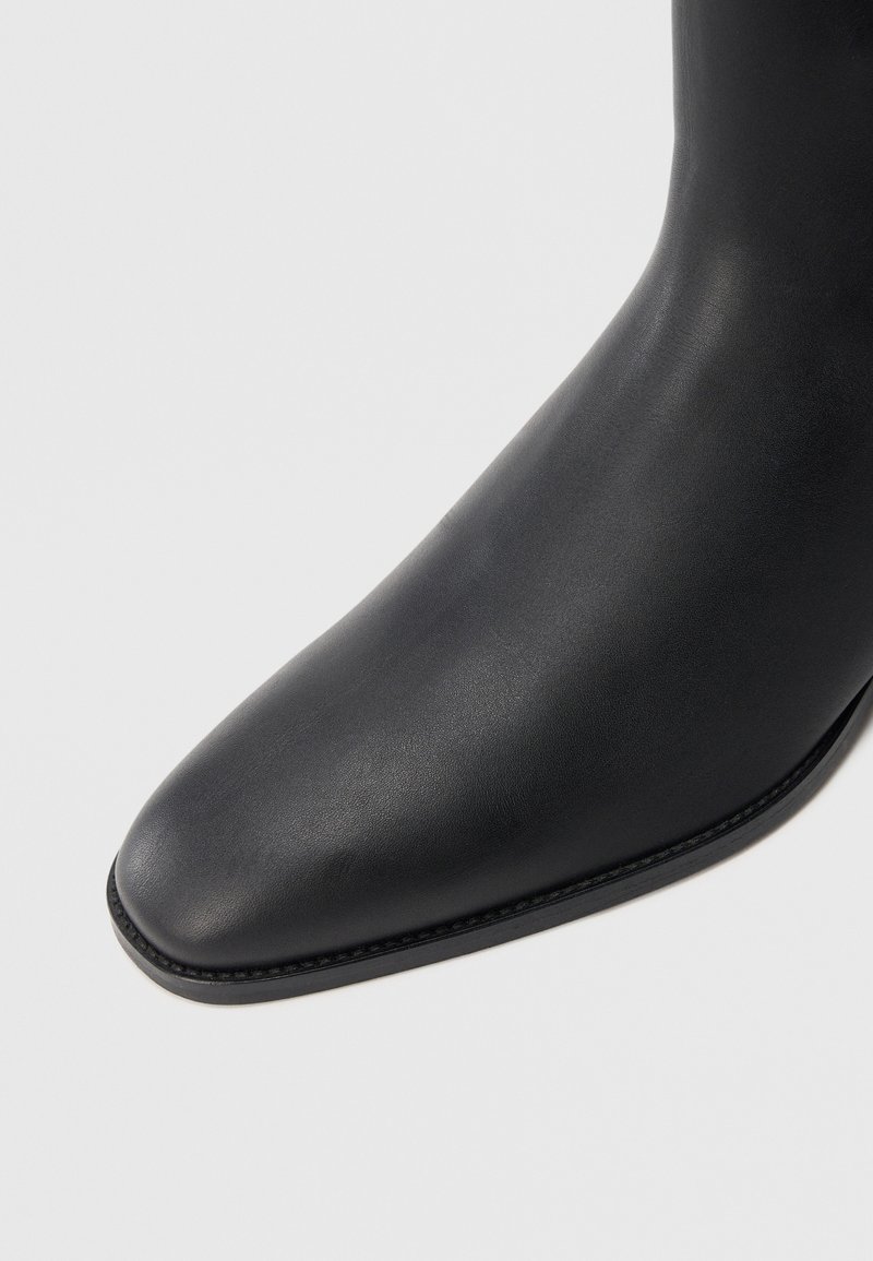 Botte en cuir lisse noir avec un bout légèrement pointu et une couture visible le long du bord de la semelle.