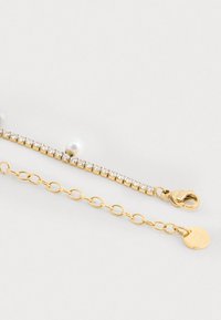 Bracciale d'oro con una fila di strass chiari e una perla bianca centrale. Presenta un'estensione a catena e una chiusura a moschettone per il bloccaggio.