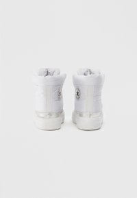Sneakers alte imbottite bianche con parte superiore in tessuto morbido, polsino elasticizzato, dettagli in hardware argentato e una toppa rotonda con logo sul lato.