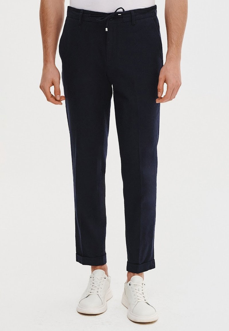 Granatowe spodnie wykonane z lekkiego materiału, z prostymi nogawkami. Posiadają elastyczny pas ze sznureczkiem, mankiety u dołu oraz boczne kieszenie.