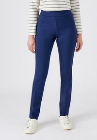 Marineblauwe stretchbroek met een hoge tailleband, twee voorklikken en een gladde textuur, gecombineerd met witte sneakers.
