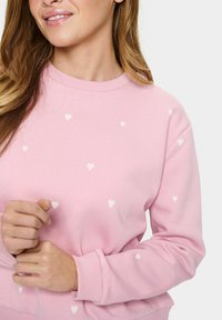 Roosa pusakas, mis on valmistatud pehmest kangast, millel on kogu pindalal väiksed valged südame mustrid; ribatud kaelus ja mansetid loovad liibuvat välimust.