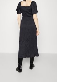 Vestido negro midi con mangas cortas abullonadas, espalda cuadrada, tejido texturizado y una silueta fluida, combinado con botas negras hasta la rodilla.