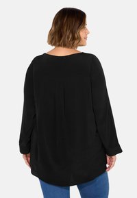 Czarna bluzka z długim rękawem, okrągłym dekoltem i detalem w postaci pliski z tyłu, wykonana z gładkiego materiału, zestawiona z niebieskimi dżinsami.