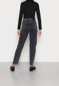 Top nero a maniche lunghe, jeans in denim grigi ad altezza vita alta, taglio dritto, tasche posteriori, abbinati a scarpe nere, design minimalista, texture liscia.