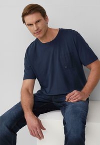 Navyblauwe t-shirt met korte mouwen en een borstzak, gemaakt van zachte stof. Gedragen met een donkere spijkerbroek, met een eenvoudig, klassiek ontwerp.