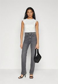 Baltas trumpomis rankovėmis viršus su gėlėtu raštu, tamsiai pilkos spalvos aukštu liemeniu džinsai, juodos basutės su dirželiais ir juoda rankinė.