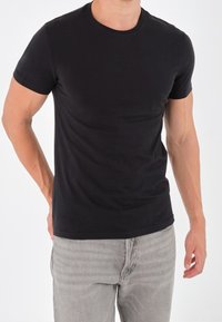 T-shirt nera a maniche corte in un design aderente, realizzata in morbido tessuto di cotone. Presenta un colletto rotondo e cuciture minime per un aspetto pulito.