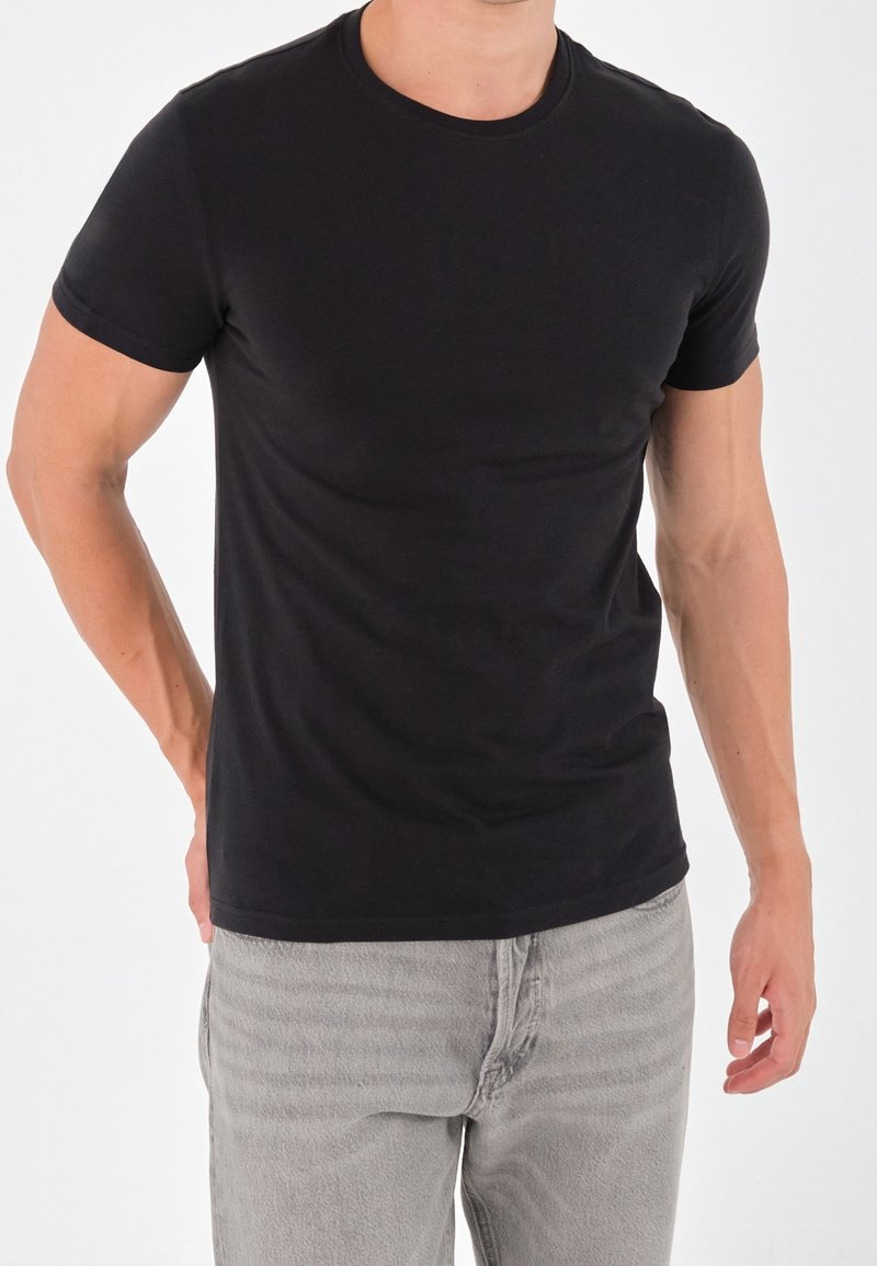 T-shirt nera a maniche corte in un design aderente, realizzata in morbido tessuto di cotone. Presenta un colletto rotondo e cuciture minime per un aspetto pulito.