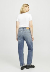 Jeans de tiro alto de color azul claro con pierna recta y bolsillos traseros. Llevados con una camiseta ajustada blanca y zapatos de plataforma negros.