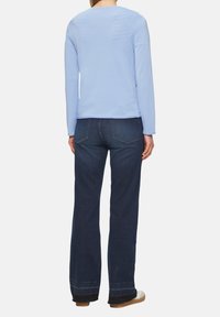 Hellblaues Langarmoberteil mit Rundhalsausschnitt, kombiniert mit dunkelblauen weiten Jeans. Weicher Stoff, minimales Design. Verstellbare Säume an den Jeans.