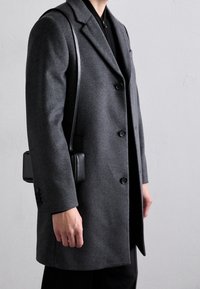 Cappotto di lana grigio con una vestibilità su misura, caratterizzato da un colletto a lappini, tre bottoni e una texture liscia; abbinato a una piccola borsa a tracolla nera.