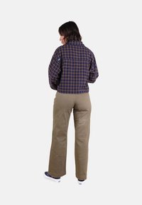 Veste en polaire à carreaux navy et jaune avec un col haut, associée à un pantalon beige et des baskets. Le design présente une coupe décontractée et un tissu texturé.