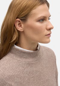 Suéter de punto acanalado marrón claro con un cuello alto y un suave color blanco debajo, presenta un corte holgado y una textura suave.